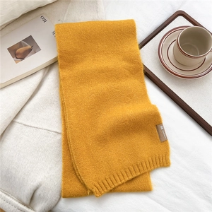 Detail of ginger yellow knit scarf with ribbed cuff and brown label on white bedding