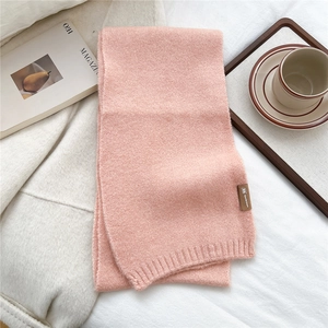 Close-up of soft light pink knit scarf texture and brown fabric brand label detail