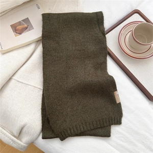 Detailed close-up of dark olive green knitted scarf texture with brand label on fabric