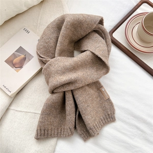 Close-up of soft camel knit scarf texture with a stylish leather logo label on white linen