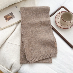 Detail of soft knit scarf with brown leather logo patch on warm textile background
