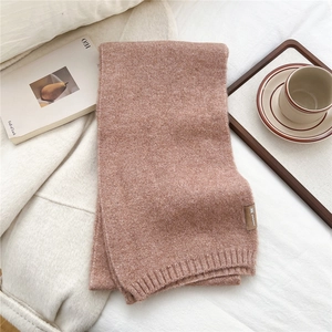 Detail of terracotta knitted scarf with ribbed edges and decorative brown leather tag