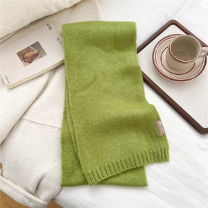 Detail of green knitted scarf showing soft texture and leather label in a cozy setting