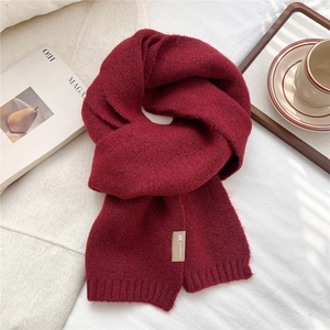 Detail of burgundy knitted scarf featuring a brown leather brand tag and ribbed edge