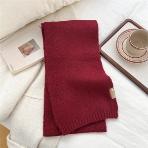 Detail of soft burgundy knitted scarf texture and premium woven label on white blanket
