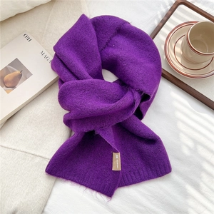 Detail of dark purple knitted scarf texture featuring plush fabric and woven brand label