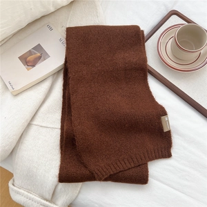 Detail view of a soft knit dark brown scarf with brand label on a cozy tray