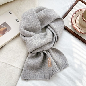 Close-up of gray knitted scarf showing ribbed edge and premium leather brand tag