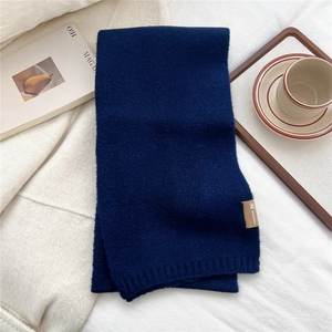 Flat lay of navy blue knitted scarf with leather brand tag and cozy winter accessories