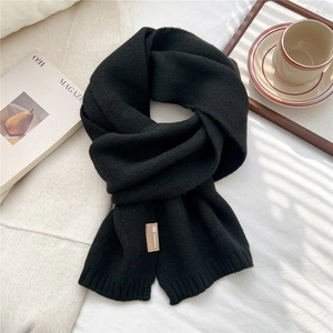 Close-up of black knit scarf with thick texture and brand label on a cozy setting