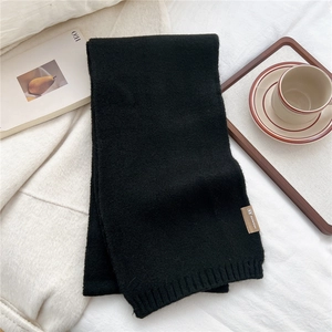 Close-up of black ribbed knit scarf with a leather label next to a coffee cup