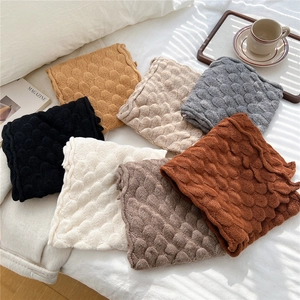 Close-up of fish scale textured knit scarves in various colors on a white bed