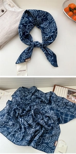 Detailed macro view of dark blue silk scarf with white rose patterns and brand tag
