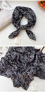 Détail d'un foulard en soie à motif plumes sur fond de chemise en lin clair