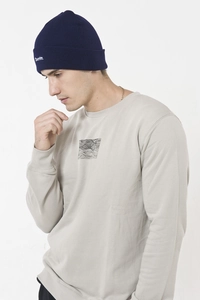 Detail of navy knit beanie with white letter embroidery worn with a grey sweatshirt