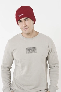 Close-up of a deep red knit beanie featuring white Brunnen artistic embroidery detail