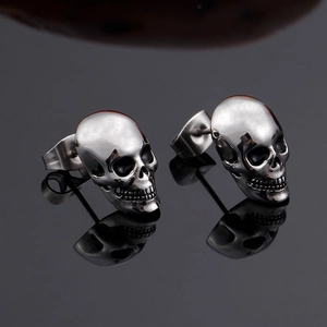 Gothic skull stud earrings for men made of polished silver titanium steel on black surface
