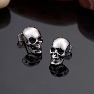 Men's titanium steel skull stud earrings with polished silver finish on reflective black surface