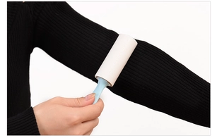 Mini portable lint roller with blue handle removing hair from black sweater sleeve