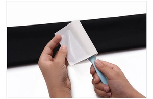Close-up of hands peeling off used sticky paper from portable blue lint roller