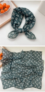 Detail of dark green paisley cotton linen scarf tied in a bow on a white surface