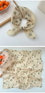Detail of light beige floral square scarf with green daisy patterns tied in a bow