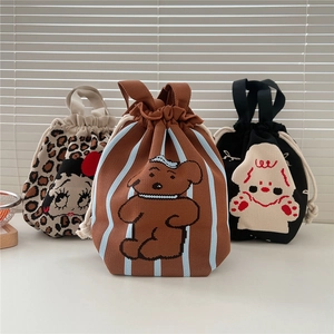 Three cute knitted drawstring handbags featuring cartoon bears and characters on a white desk
