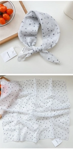 Detailed view of white polka dot cotton scarf with brand tag and lightweight texture