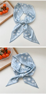 Close-up of sky blue silk scarf with white polka dots tied in a knot on a cream surface