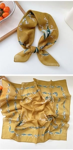Detailed pattern of yellow floral silk scarf with lily of the valley on a wooden tray