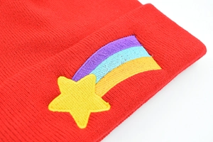 Red acrylic knit beanie featuring yellow star and rainbow embroidery in a close-up view