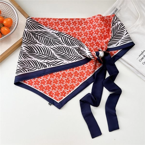 Dettaglio di un foulard in raso a fiori con bordi blu scuro e una grande fibbia a perla