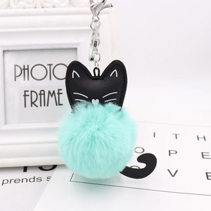 Close-up of black cat plush keychain with mint green faux fur pompom and silver metal clasp