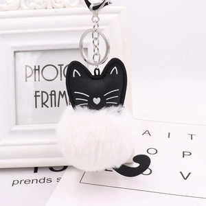 Close-up of a cute black cat keychain with a white faux fur pom-pom on a bright background