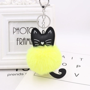 Detail of cute black cat plush keychain with a bright yellow faux fur ball and metal ring