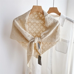 Detailed close-up of beige knitted triangle scarf with floral openwork texture on a hanger
