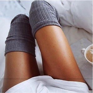 Detail of dark grey ribbed knit over-knee socks in a cozy home setting with a coffee cup