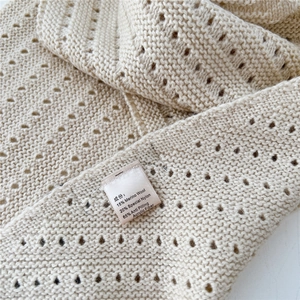Detail view of cream knit scarf showing premium merino wool blend texture and fabric care label