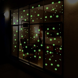Luminous snowflake and star wall stickers glowing green on a window in a dark cozy bedroom