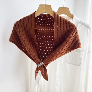 Close-up of reddish-brown knitted scarf showing diamond cutout texture and brand label