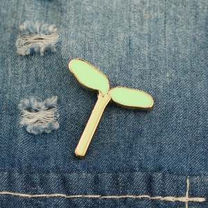 Dettaglio macro di una spilla a foglia smaltata verde con bordo dorato su denim