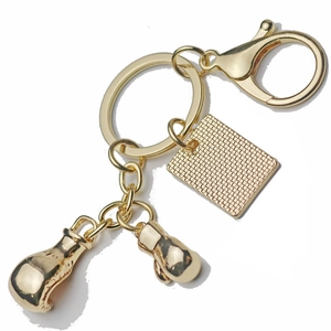 Golden boxing gloves keychain with textured metal plate accessory on white background