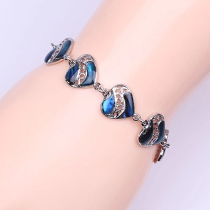 Detalle de una pulsera de corazón plateada con incrustación de concha azul puesta en muñeca