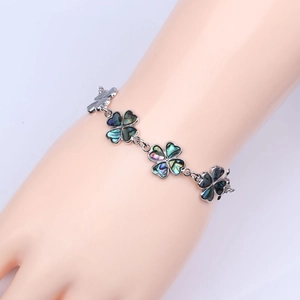 Primer plano de una pulsera de trébol plateada con concha de abulón de colores en la muñeca