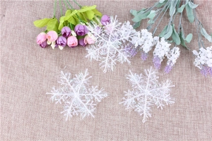 Three white Christmas snowflake ornaments with glitter on a rustic burlap background