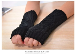Close-up of black cable-knit arm warmers with diamond jacquard pattern on a wooden desk