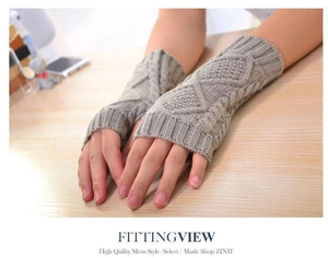 Detail view of light grey cable knit fingerless gloves on a wooden table surface