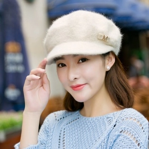 Detail view of plush beige newsboy hat with a golden metallic M letter decoration