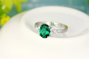 Detailed macro view of an oval emerald green gemstone ring with white side diamonds