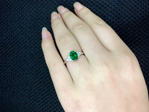 Macro detail of oval emerald green gemstone ring with side diamond accents on finger